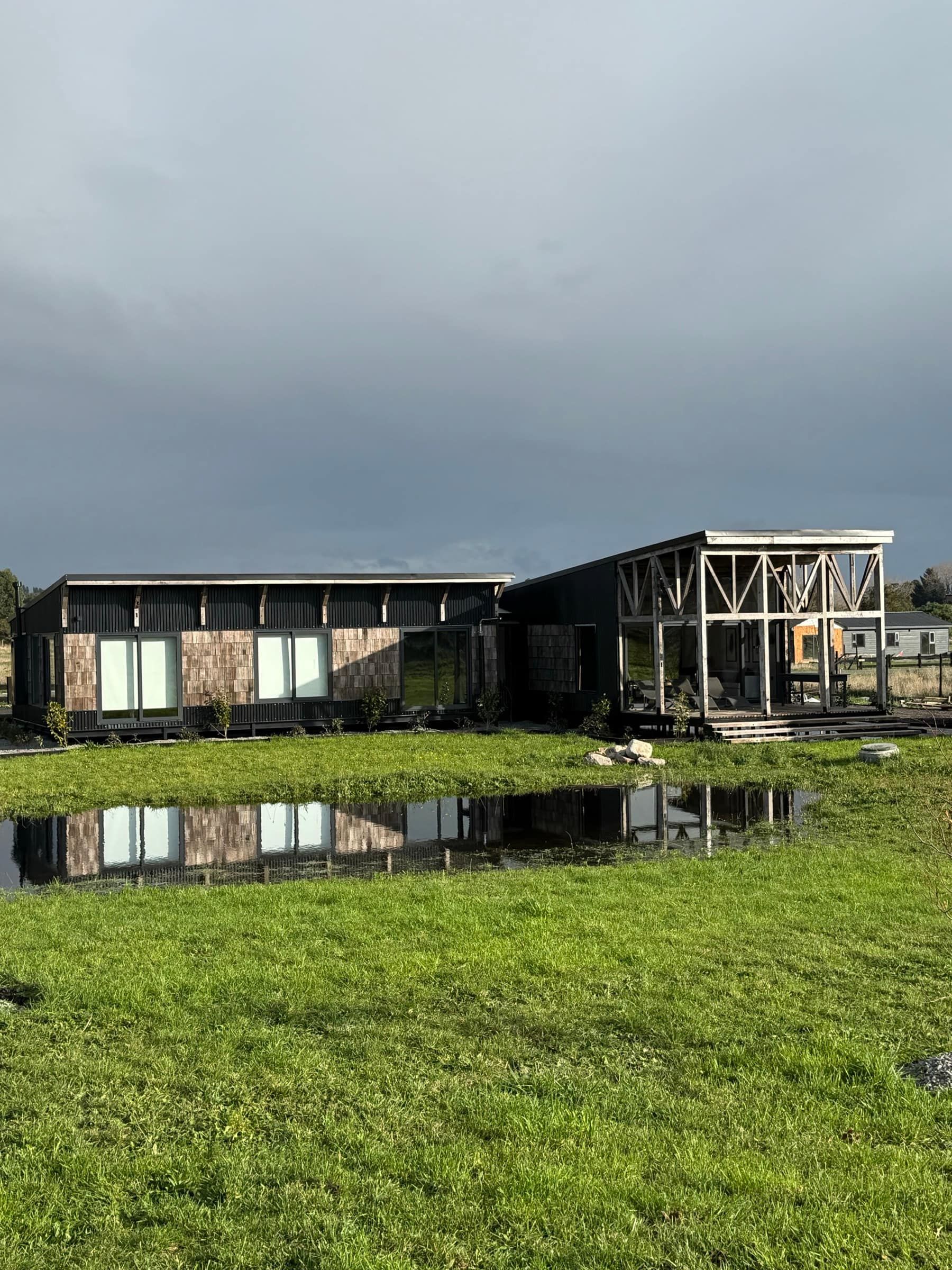 La casa de fachada oscura reflejada en el agua de la pradera, bajo el cielo del sur