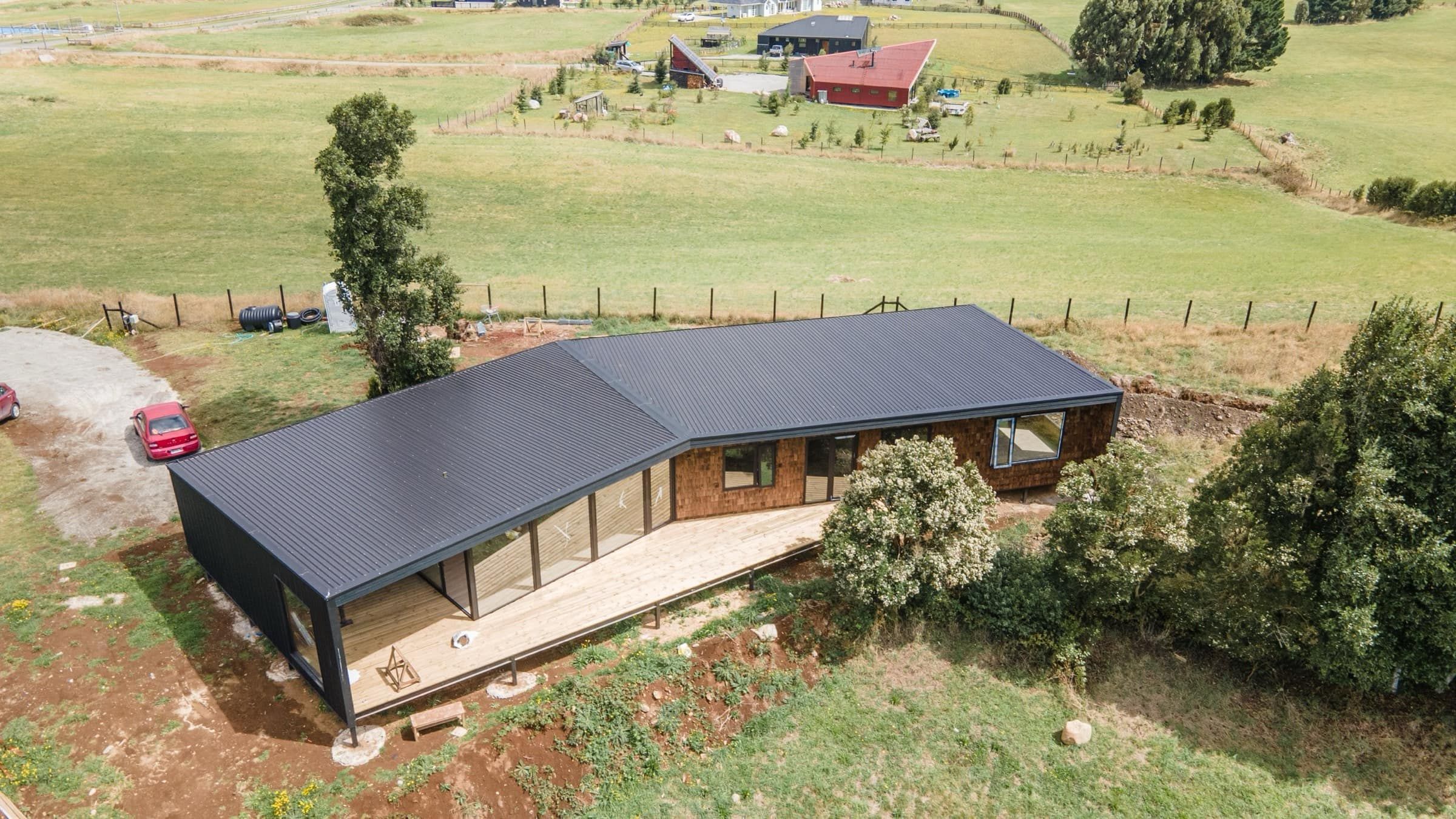 La casa de tejuela y zinc negro sobre la loma, con su terraza de madera